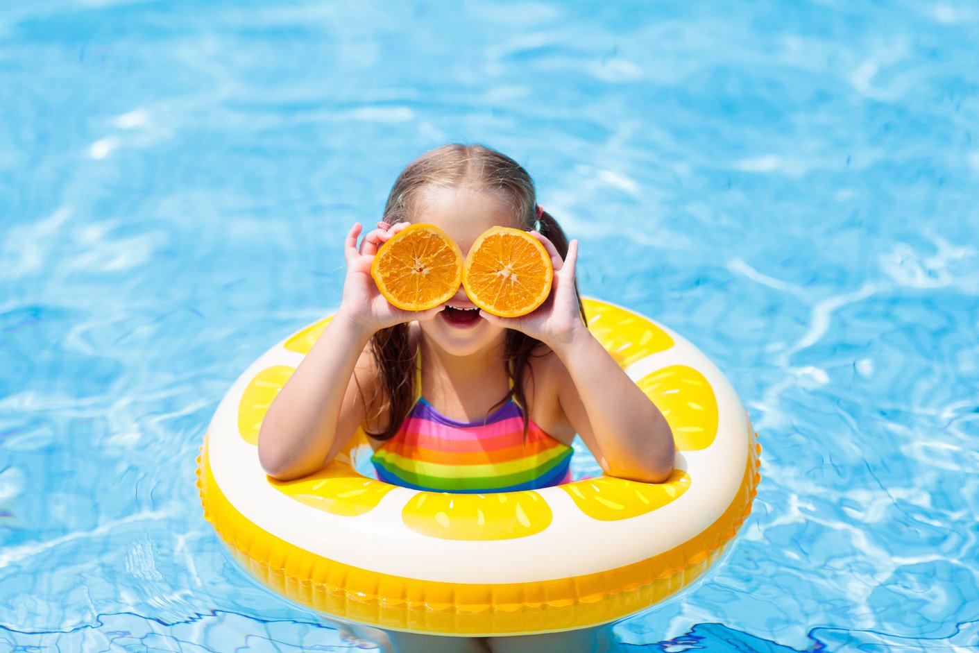 Child in swimming pool. Kid eating orange.